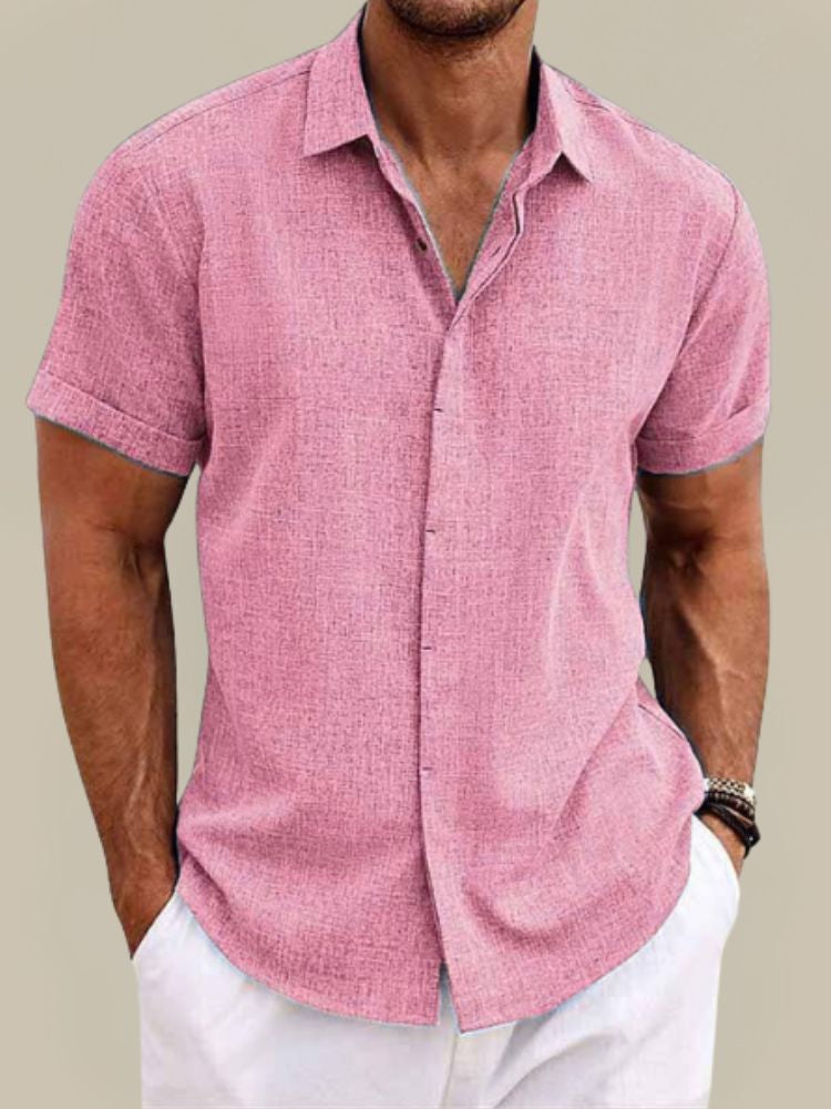 Homme portant la chemise rose à manches courtes retroussées, col ouvert et tissu texturé, avec un pantalon blanc. 7