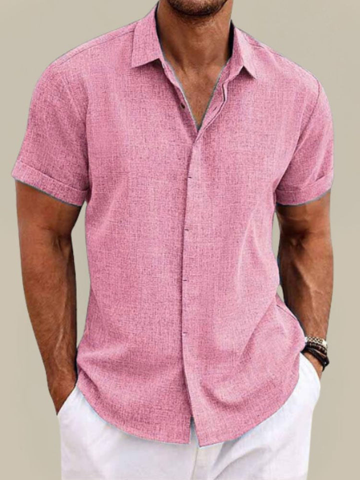 Homme portant la chemise rose à manches courtes retroussées, col ouvert et tissu texturé, avec un pantalon blanc. 7