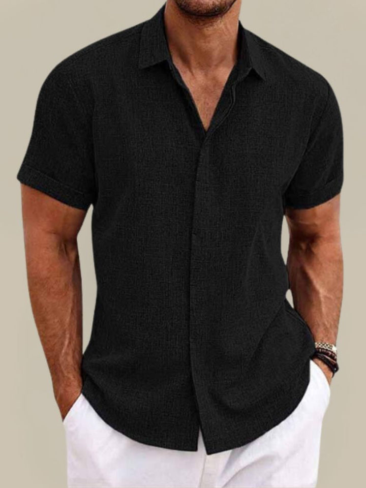 Chemise noire à manches courtes boutonnée sur le devant, portée par un homme avec un pantalon blanc, vue de face. 6