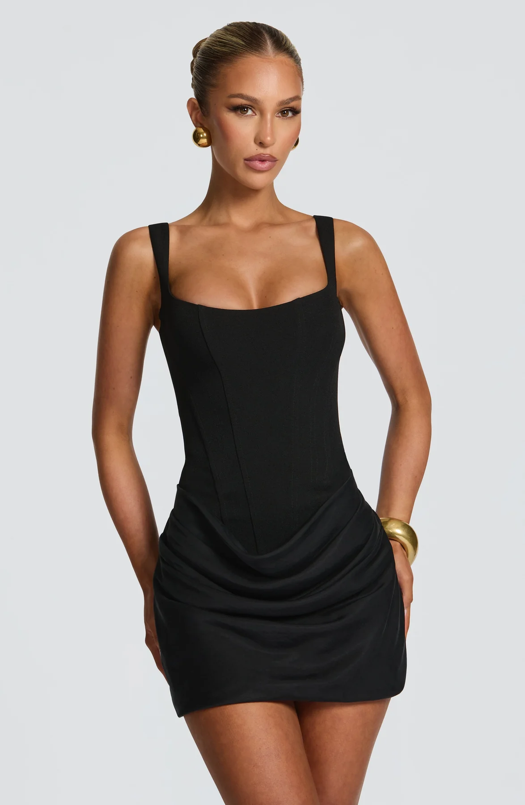 Gros plan de face sur la version noire de la robe, bustier structuré à larges bretelles et jupe drapée, avec boucles d'oreilles dorées. 5