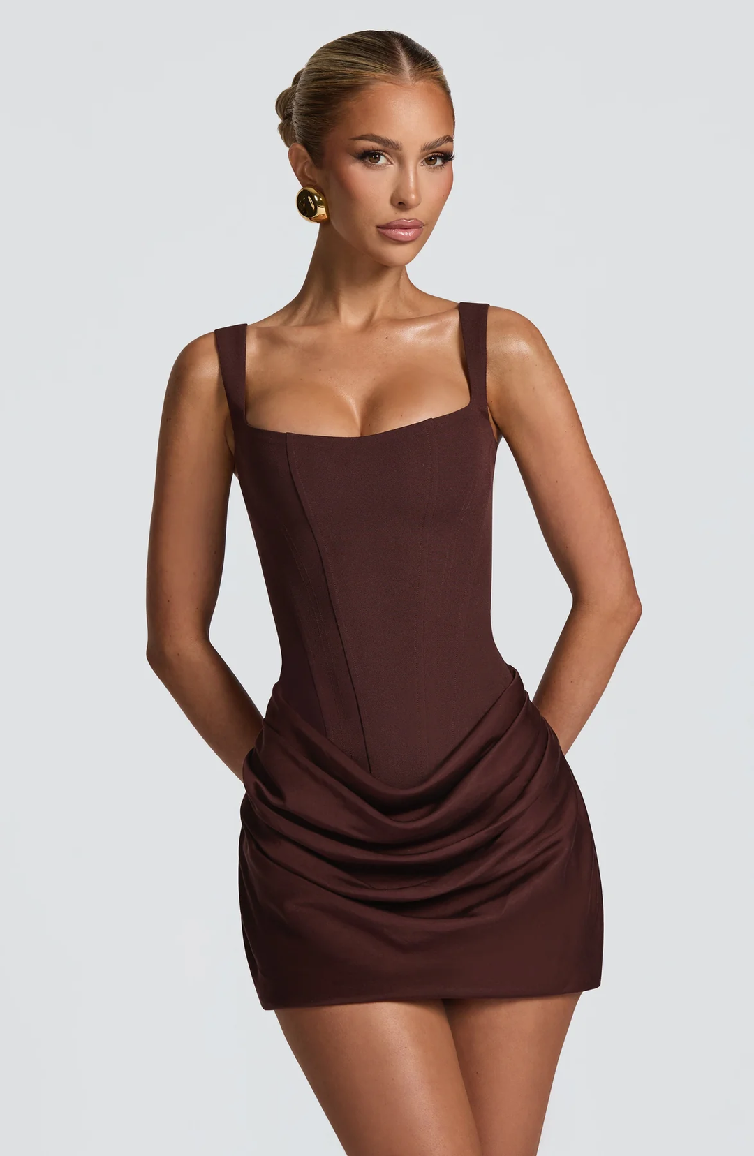 Gros plan de face sur la version marron chocolat de la robe, bustier à coutures apparentes et jupe drapée, boucle d'oreille dorée. 9