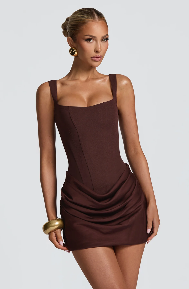 Robe marron chocolat portée de trois quarts, buste et jupe en gros plan, avec large bracelet doré et jupe drapée sur le côté. 11