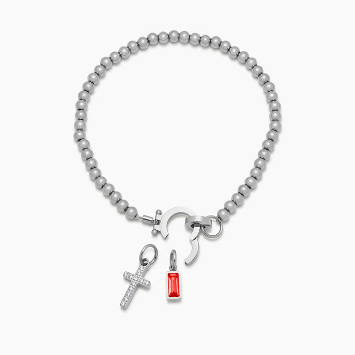 Bracelet argenté à perles, fermoir ouvert, avec la croix de strass et la pierre rouge présentées séparément en dessous. 10