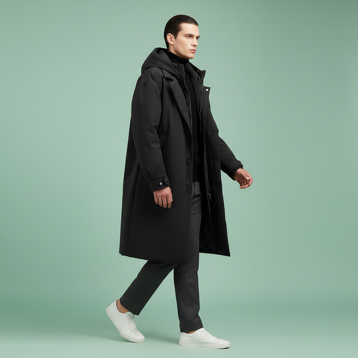 Homme en marche vu de côté, manteau noir ouvert à capuche, pantalon gris foncé et baskets blanches. 7