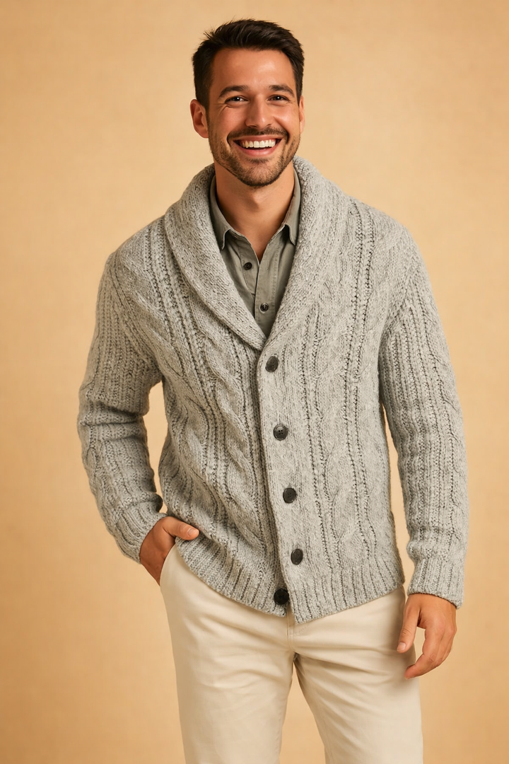 Homme souriant en cardigan gris clair chiné à torsades épaisses et col châle, sur une chemise vert kaki, une main dans la poche. 7