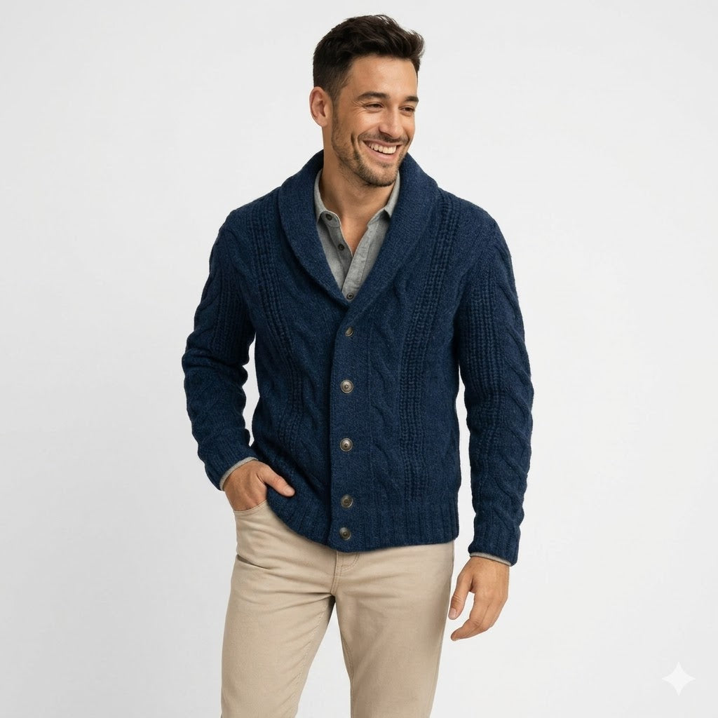Homme souriant en cardigan bleu marine à torsades et col châle, porté sur une chemise grise et un pantalon beige, plan taille. 1