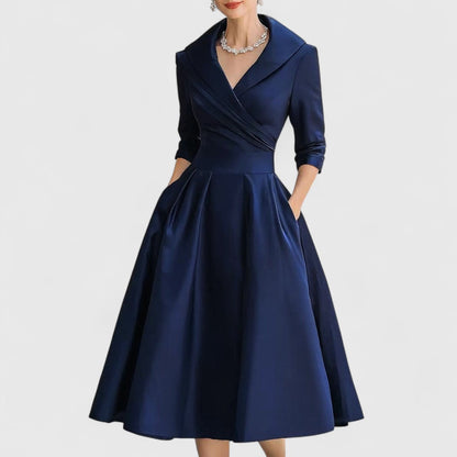 Même robe en bleu marine portée de face, col châle plissé, jupe évasée, mains dans les poches. 2