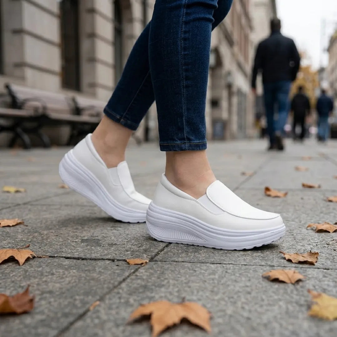Jambes de femme en jean portant les mocassins blancs, marchant sur un trottoir parsemé de feuilles 11