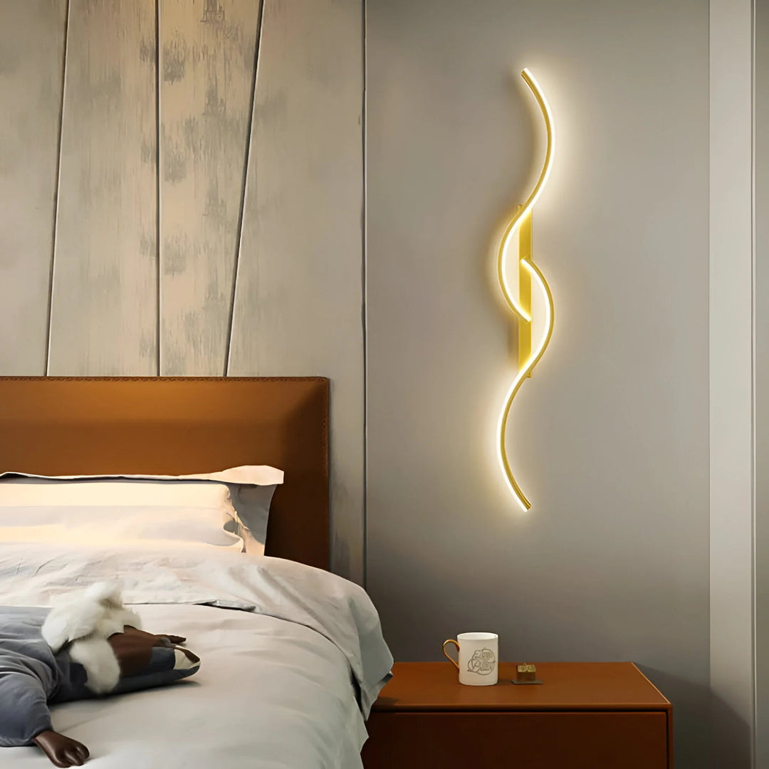 Applique dorée aux courbes lumineuses fixée au mur d'une chambre, à côté d'une table de chevet 2