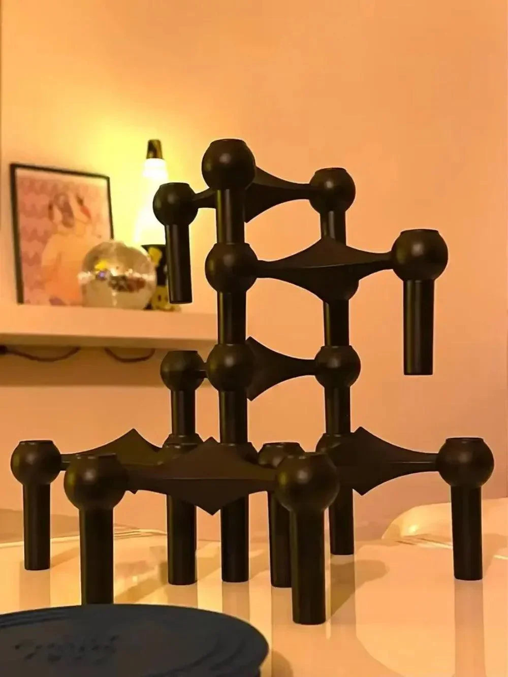 Modules noirs mats empilés en tour sur une surface claire, dans un intérieur éclairé de lumière chaude. 3