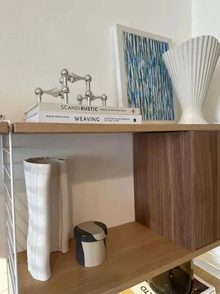 Porte-bougie argenté assemblé sur une pile de livres, sur une étagère en bois avec vases et tableau bleu. 4