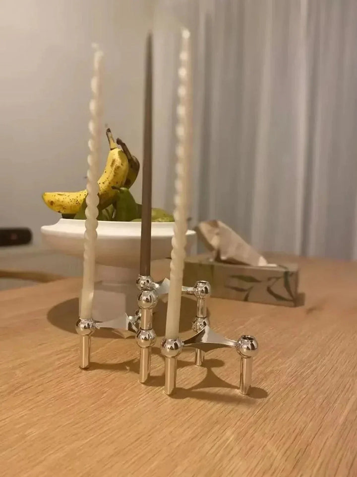 Deux modules argentés assemblés avec des bougies longues, blanches et marron, sur une table en bois près d'une corbeille de fruits. 5