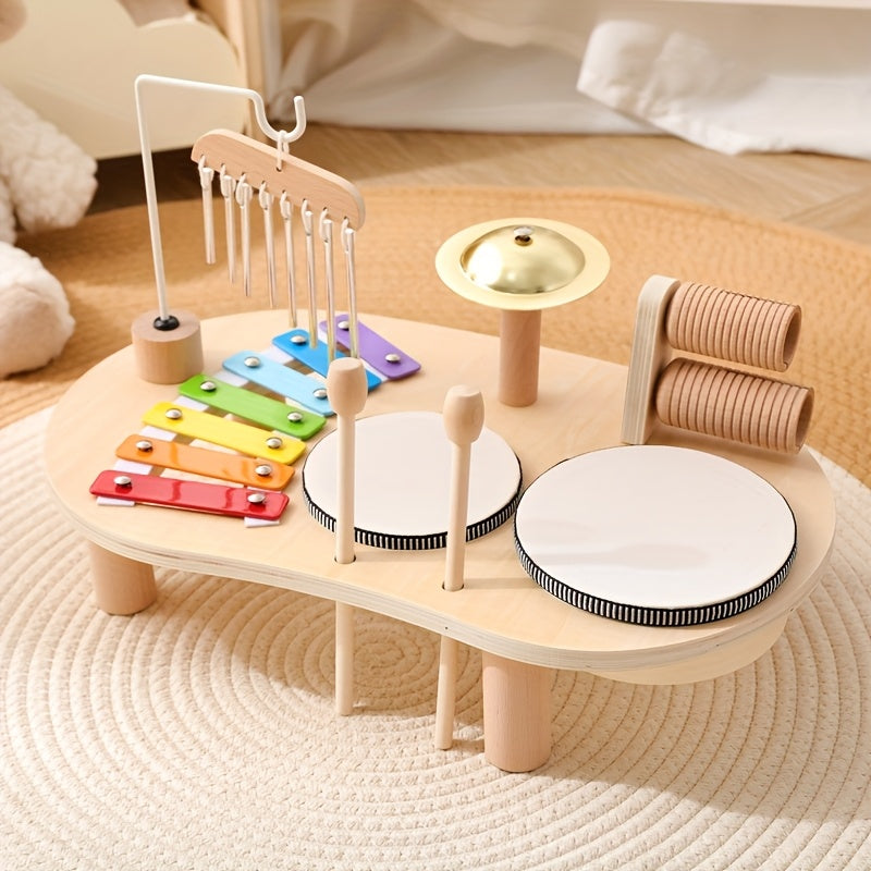 Table musicale en bois posée sur un tapis rond, avec xylophone arc-en-ciel, carillon, cymbale dorée, deux tambours et maracas en bois. 1