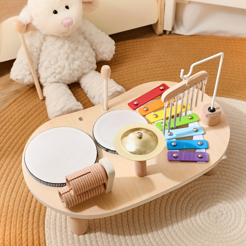 Table musicale vue de dessus côté tambours, avec xylophone coloré, carillon et cymbale, posée sur un tapis tressé devant une peluche. 4