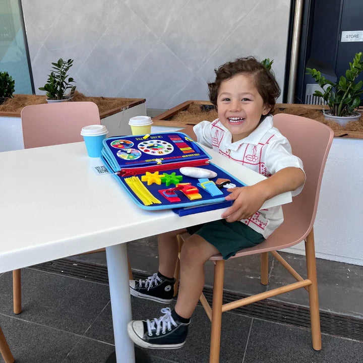 Petit garçon rieur attablé à une terrasse, le livre bleu ouvert devant lui sur la table 7