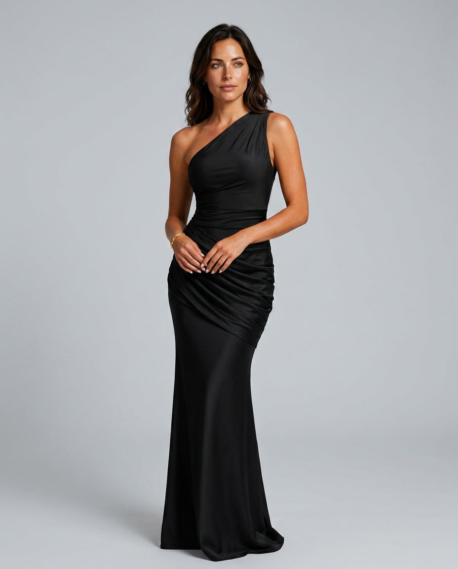 Vue de face de la robe noire portée par une mannequin, mains jointes devant elle, drapé en biais sur la hanche. 1