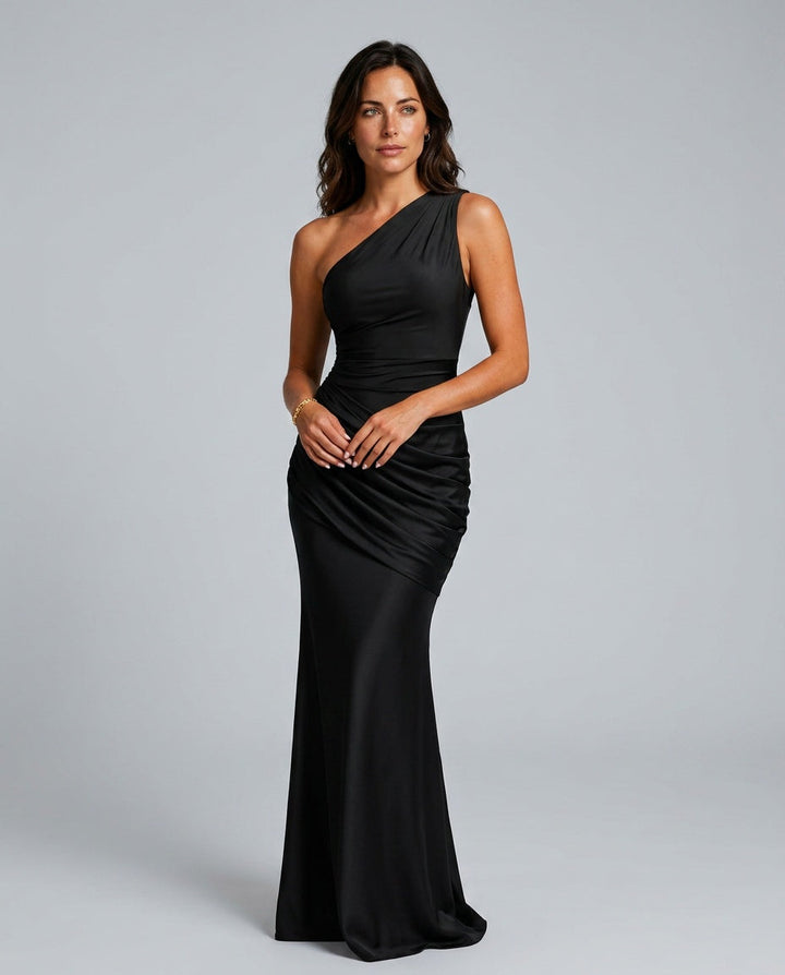 Vue de face de la robe noire portée par une mannequin, mains jointes devant elle, drapé en biais sur la hanche. 1