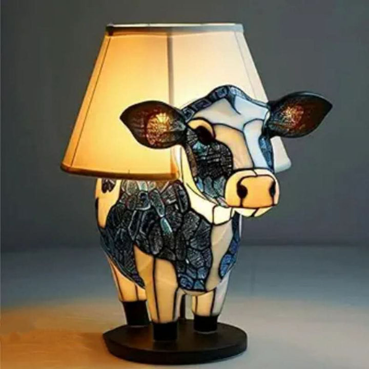 Lampe en forme de vache à robe bleu et blanc, posée sur un socle rond et coiffée d'un abat-jour en tissu allumé. 12
