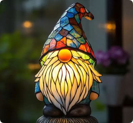 Veilleuse en forme de gnome à longue barbe blanche et bonnet pointu en vitrail bleu, vert et orange, éclairée devant un fond flou. 13