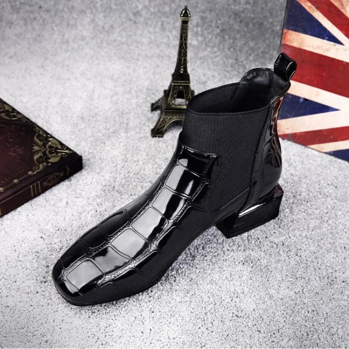 Boot noire vernie à motif croco et empiècement élastique, vue de trois quarts avant, posée sur une moquette grise près d'une mini tour Eiffel. 1