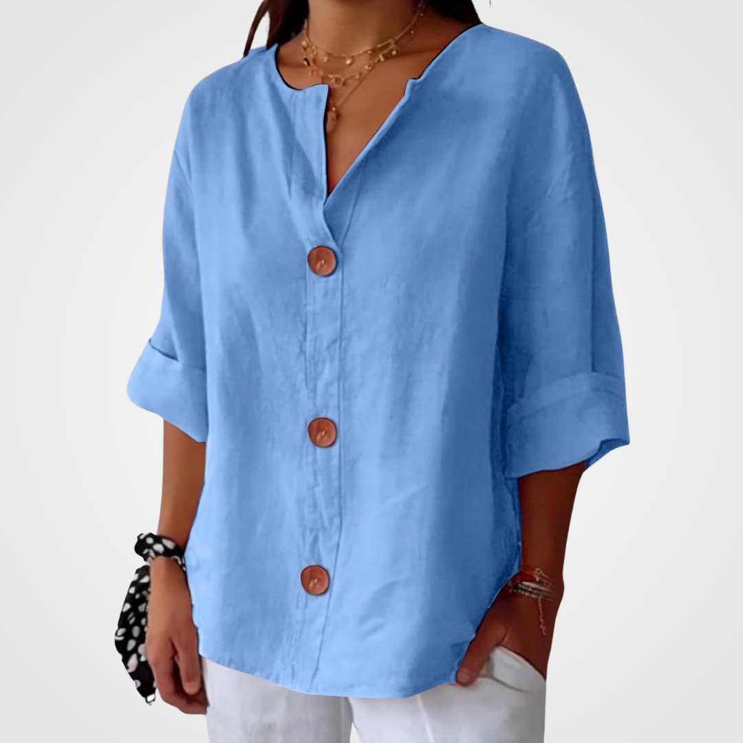 Blouse bleu ciel portée sur fond blanc uni, cadrage du buste aux hanches, boutons en bois et manches trois-quarts retroussées. 14