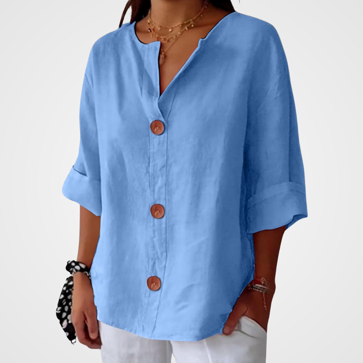 Blouse bleu ciel portée sur fond blanc uni, cadrage du buste aux hanches, boutons en bois et manches trois-quarts retroussées. 14
