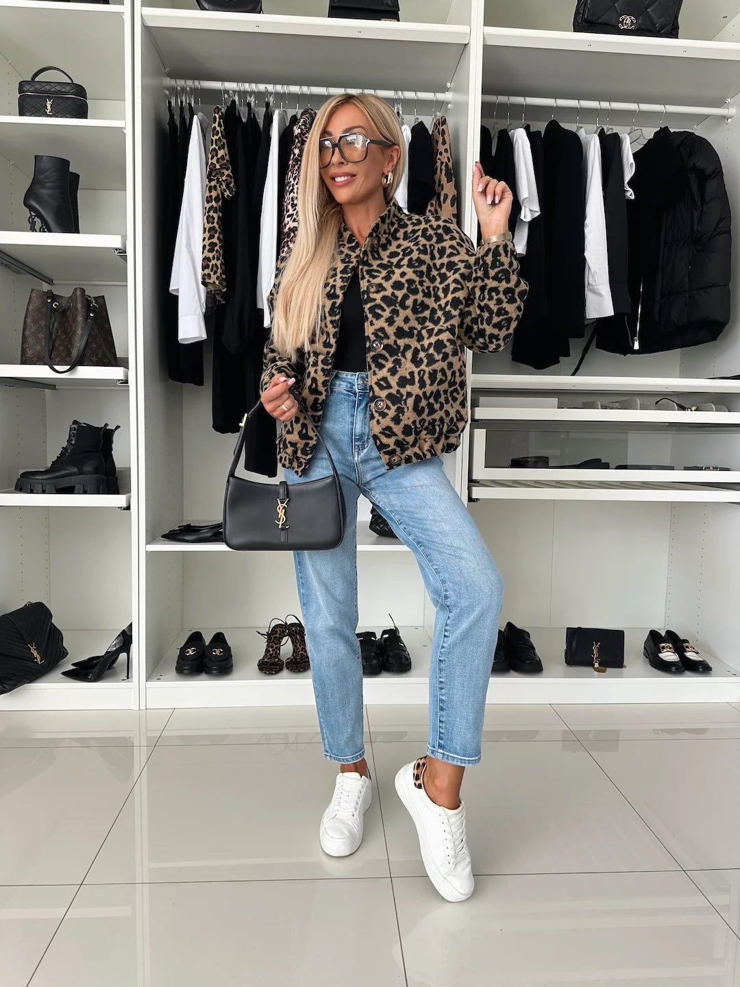 Look complet en pied : veste bomber léopard, haut noir, jean clair et baskets blanches, devant un dressing aux étagères blanches. 5