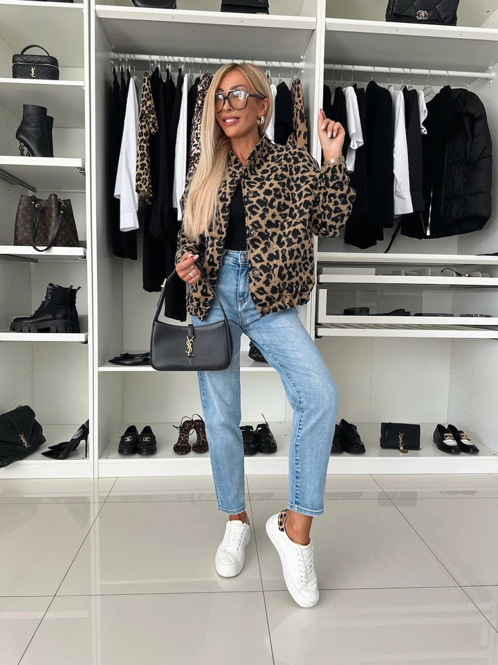 Look complet en pied : veste bomber léopard, haut noir, jean clair et baskets blanches, devant un dressing aux étagères blanches. 5