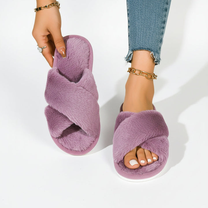 Chaussons mauves à brides croisées en peluche, un porté avec un jean et l'autre tenu à la main pour montrer la semelle intérieure. 8