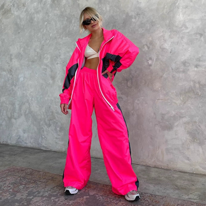 Modèle en ensemble rose fluo à empiècements gris foncé, veste zippée ouverte sur un haut blanc, main sur la hanche. 8