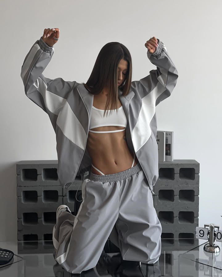 Modèle agenouillée bras levés, ensemble gris à larges bandes blanches, veste zippée ample et pantalon large à taille élastique. 20