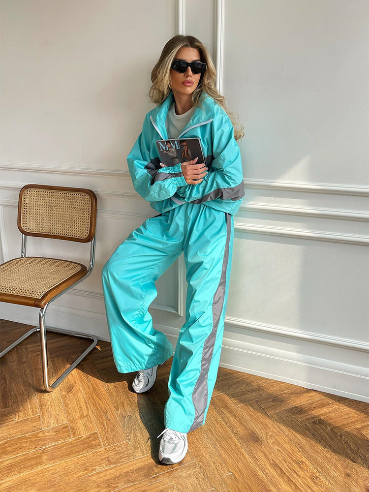 Modèle adossée au mur, ensemble turquoise à bandes grises, magazine contre la poitrine, chaise cannée à côté. 11