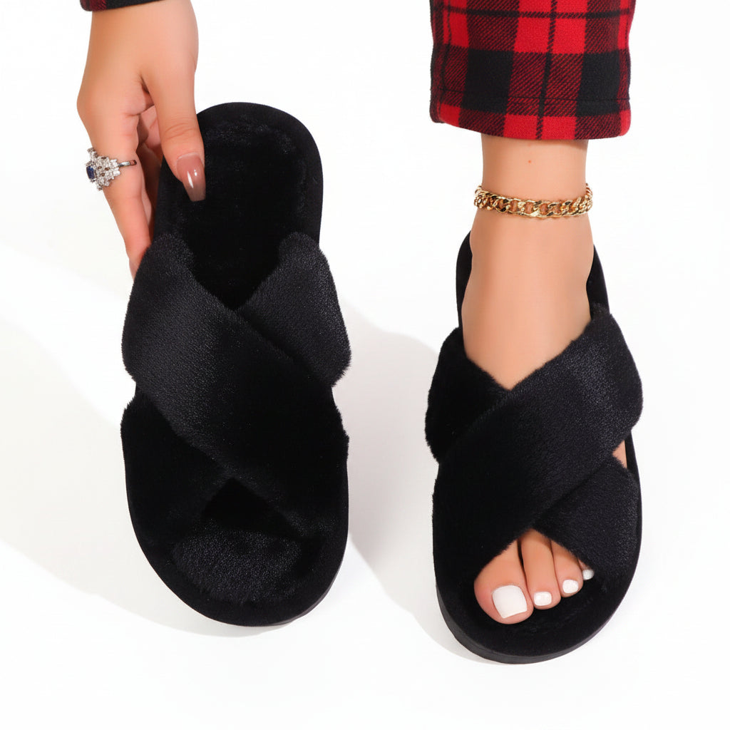 Chaussons noirs à brides croisées en peluche, un porté avec un pantalon à carreaux rouges et noirs, l'autre tenu à la main. 9