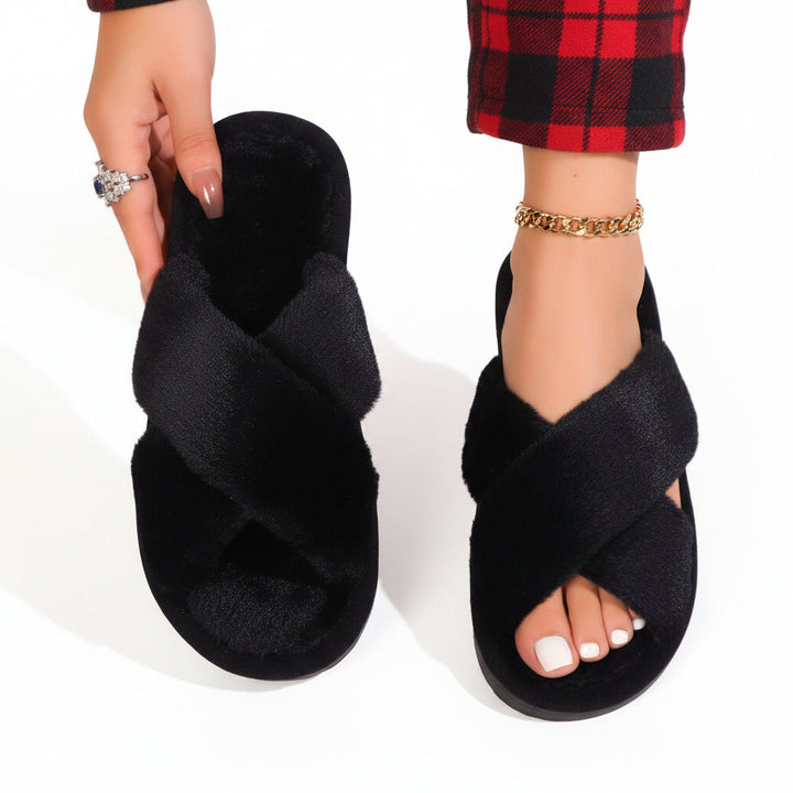 Chaussons noirs à brides croisées en peluche, un porté avec un pantalon à carreaux rouges et noirs, l'autre tenu à la main. 9