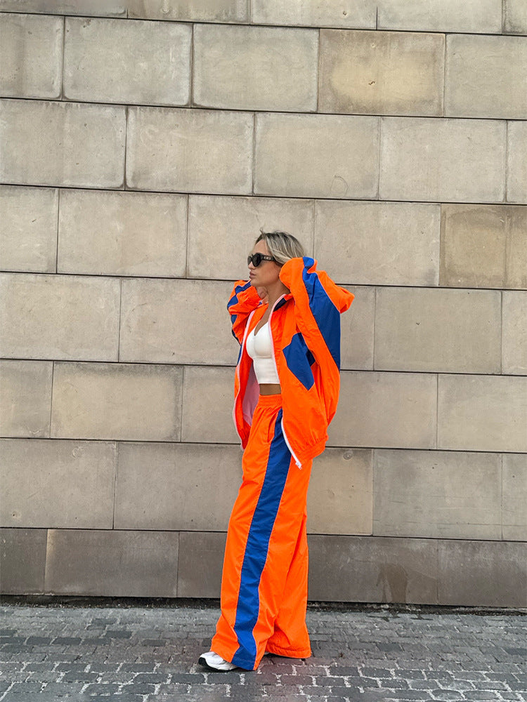 Modèle de profil devant un mur de pierre, ensemble orange vif à empiècements bleus, veste ouverte et pantalon large. 15