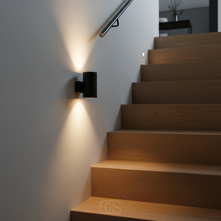 Gros plan sur une veilleuse noire au mur d'une cage d'escalier en bois, lumière chaude en cône au-dessus et en dessous. 5