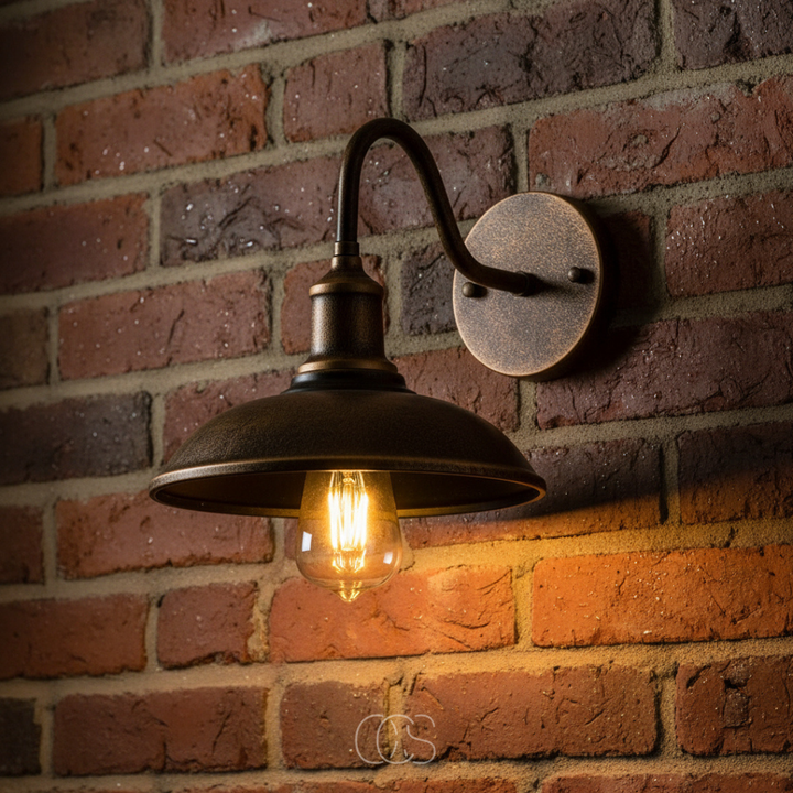 Gros plan sur l'applique bronze vieilli, sa platine ronde et son ampoule à filament, fixées sur un mur de briques rouges. 5