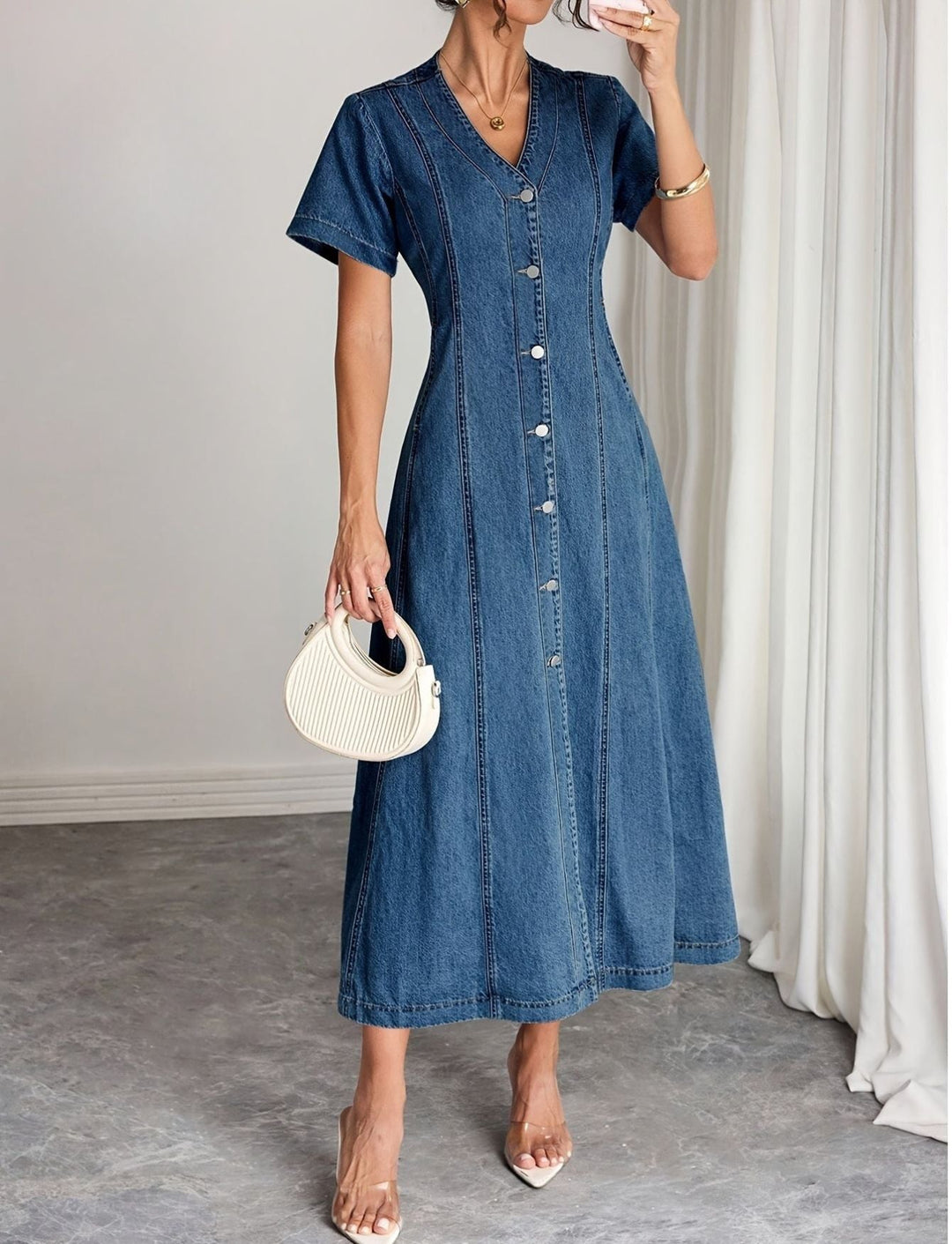 Robe longue boutonnée à col en V portée par une femme tenant un petit sac crème 1