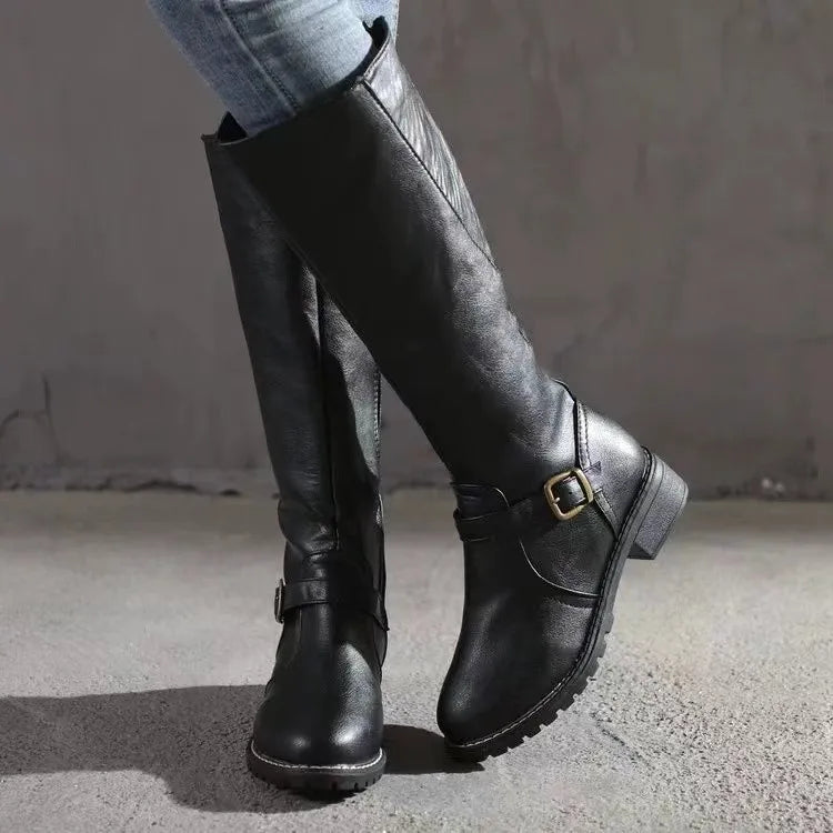 Bottes hautes noires portées en marche, vue de trois quarts avec la boucle dorée sur le côté et le talon bas. 2