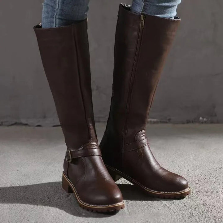 Bottes hautes marron foncé portées avec un jean, vue de face montrant la fermeture éclair latérale et la sangle à boucle. 3
