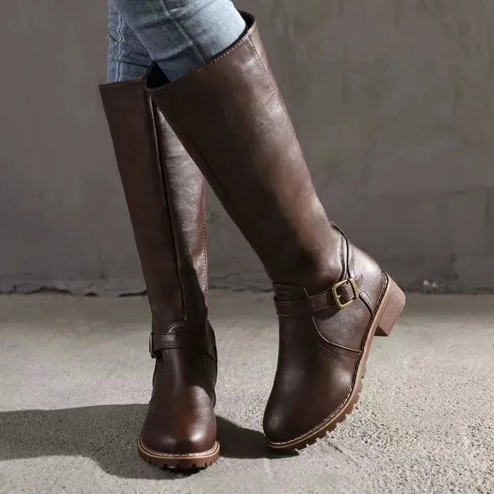Bottes hautes marron foncé portées en marche, vue de trois quarts avec la boucle dorée et la semelle crantée. 4