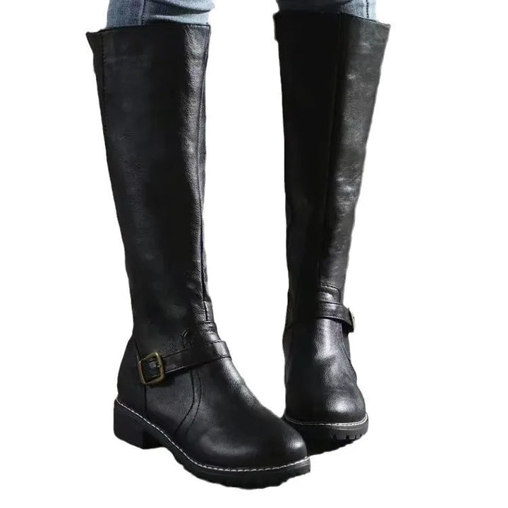 Bottes hautes noires sur fond blanc, portées avec un jean, montrant la boucle de cheville et la semelle épaisse. 5