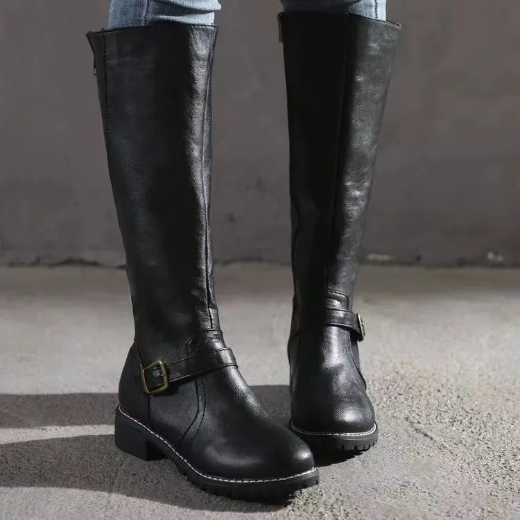 Bottes hautes noires portées avec un jean, vue de face sur sol en béton, avec boucle de cheville et talon carré. 7