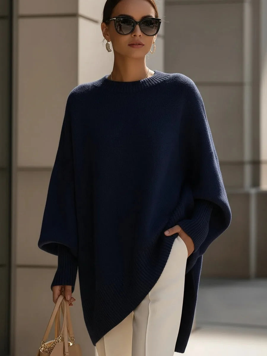 Pull bleu marine oversize à manches amples et ourlet asymétrique, porté avec un pantalon blanc et des lunettes de soleil. 8