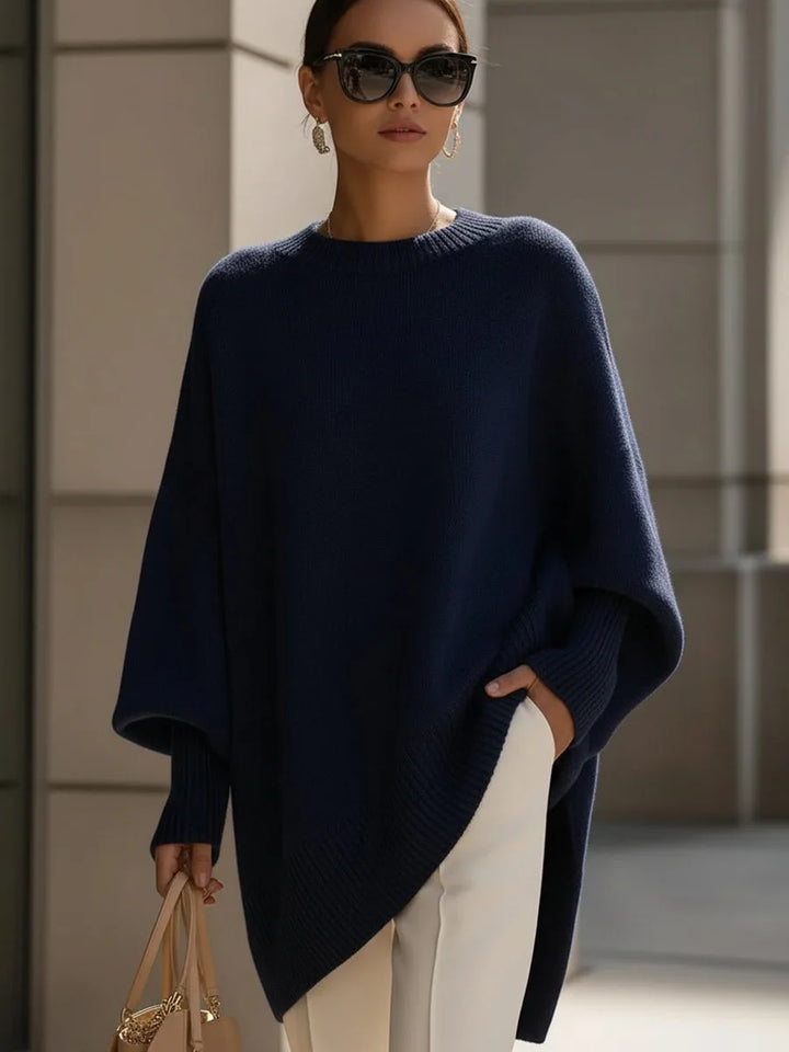 Pull bleu marine oversize à manches amples et ourlet asymétrique, porté avec un pantalon blanc et des lunettes de soleil. 8