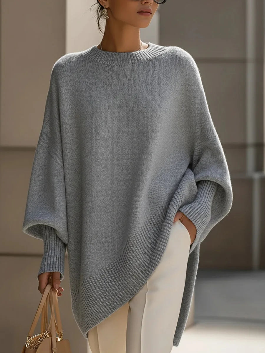 Pull gris clair oversize à ourlet asymétrique côtelé, porté avec un pantalon blanc et un sac beige. 9