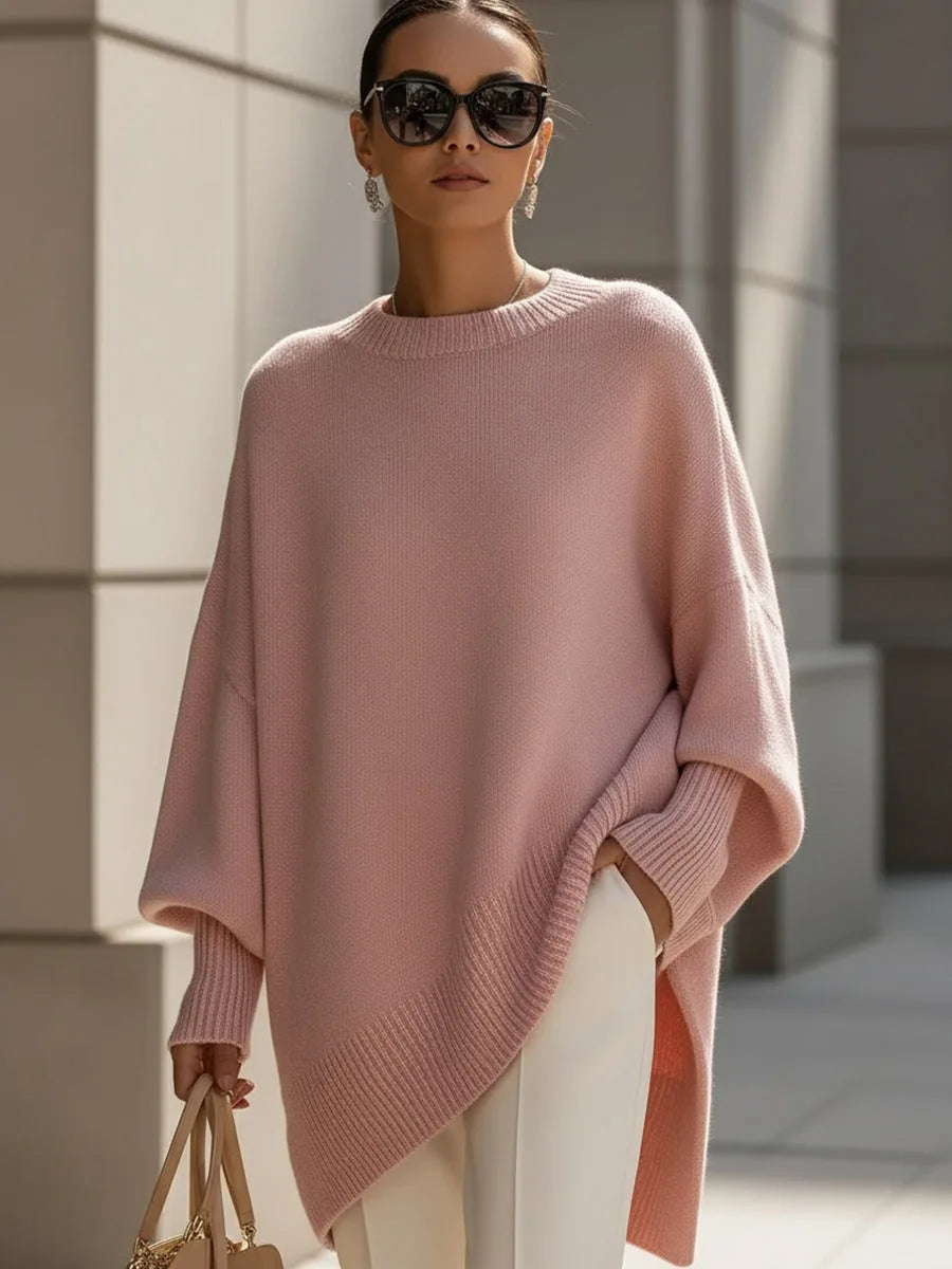 Pull rose poudré oversize à ourlet asymétrique, porté avec un pantalon blanc, lunettes de soleil et sac beige. 11