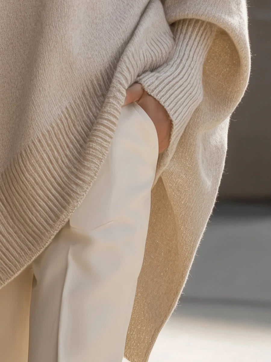 Gros plan sur la fente latérale du pull beige à l'intérieur légèrement pailleté, main dans la poche du pantalon blanc. 5