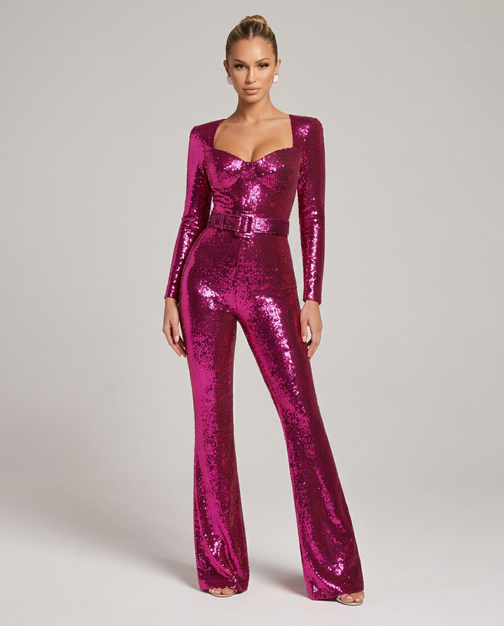Vue de face de la combinaison rose fuchsia à sequins, portée debout par un mannequin, avec ceinture assortie et jambes évasées. 1