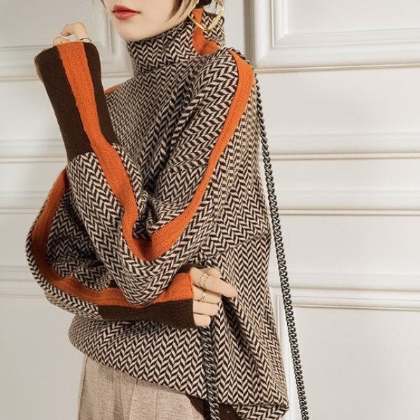 Gros plan sur les manches du pull à chevrons marron avec bandes orange, porté bras croisés, sac à chaîne sur l'épaule. 3